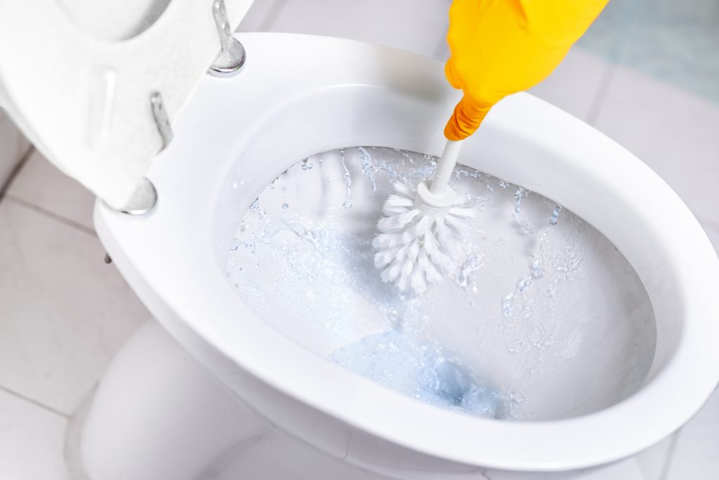 Someone wearing rubber gloves cleans a toilet basin using antibacterial wash and a toilet brush