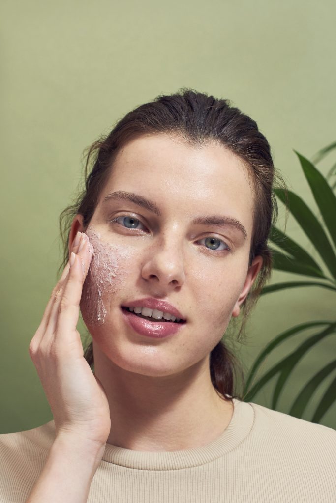 Girl cleans her face with pink exfoliating face cream