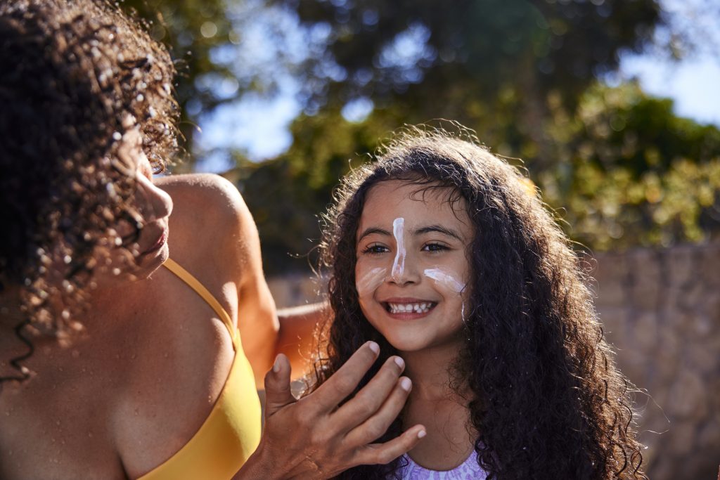 Woman puts suncream on her smiling daughter