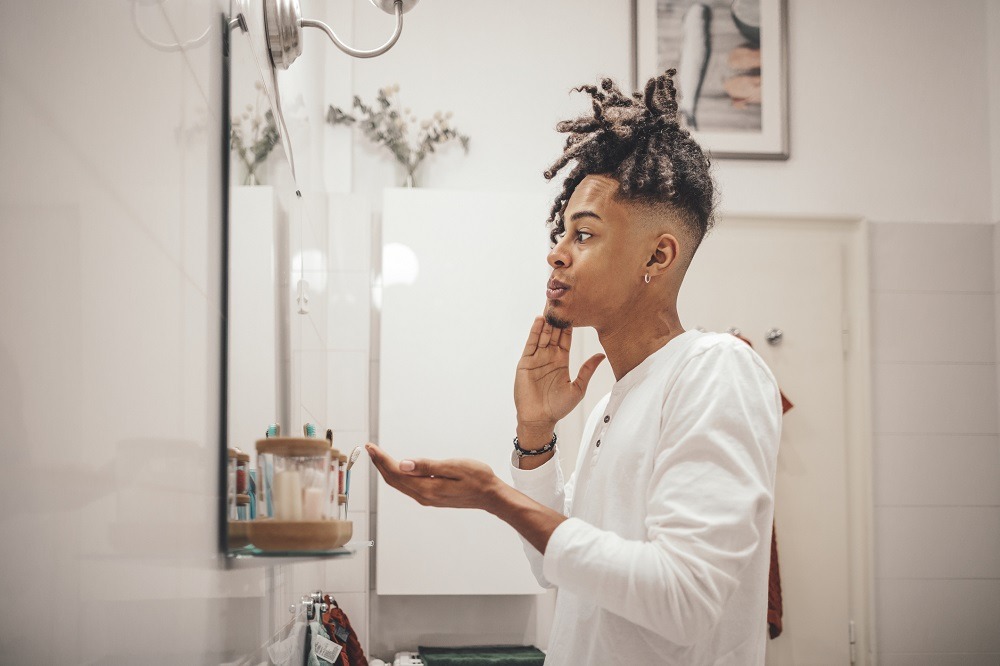 Man moisturises his face in front of the bathroom mirror