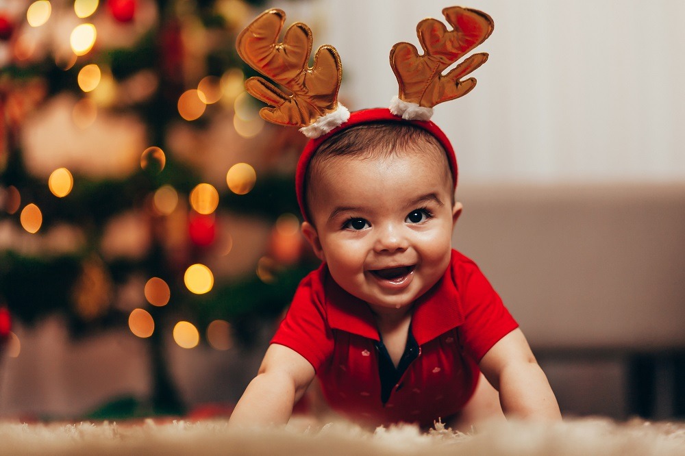 Young baby dressed in reindeer horns crawls on a carpet smiling