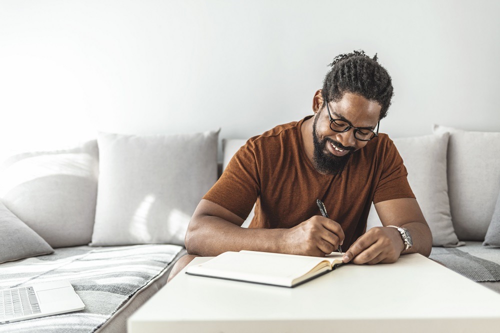 Man sits on a sofa writing in his journal