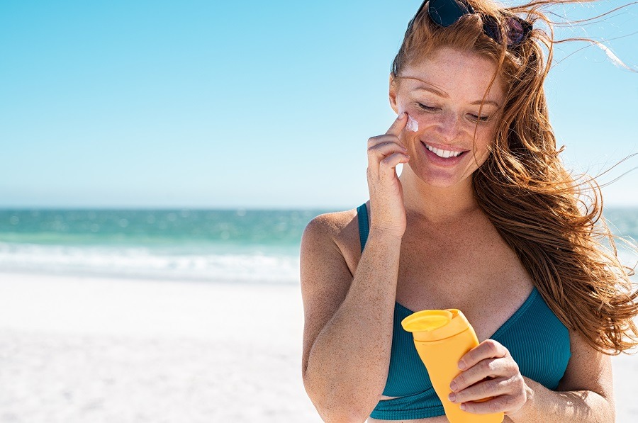 Woman on beach applies suncream to face 