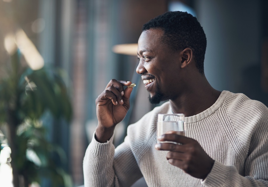 Man is about to swallow a vitamin holding a glass of water