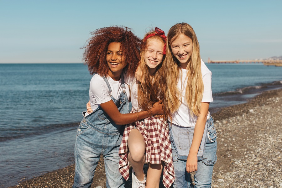 Three teenage girls laugh together on the beach