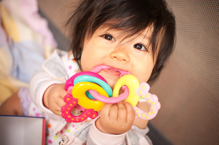 Baby girl chews colourful toy as she's teething