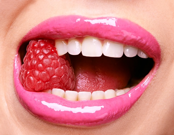 Bright pink lipstick on woman chewing a raspberry