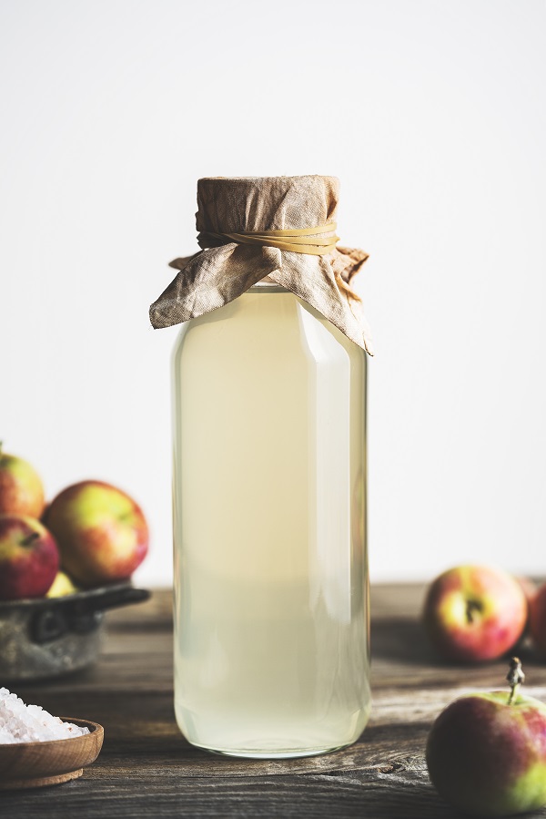 A large glass bottle of apple cider vinegar on a wooden tabletop.