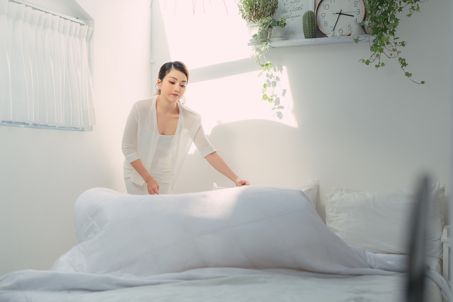 woman making her bed and changing the white sheets 