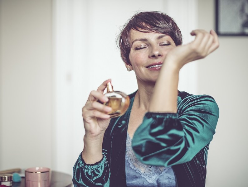 Women smelling perfume on her wrist whilst smiling.