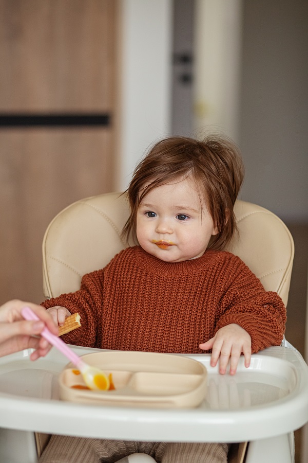 baby in high chair being fed food with a spoon