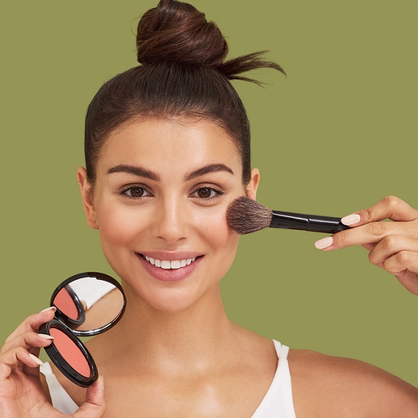 smiling model applying blusher to cheeks