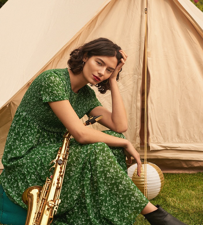 lady looking at the camera outside a tent holding a saxophone