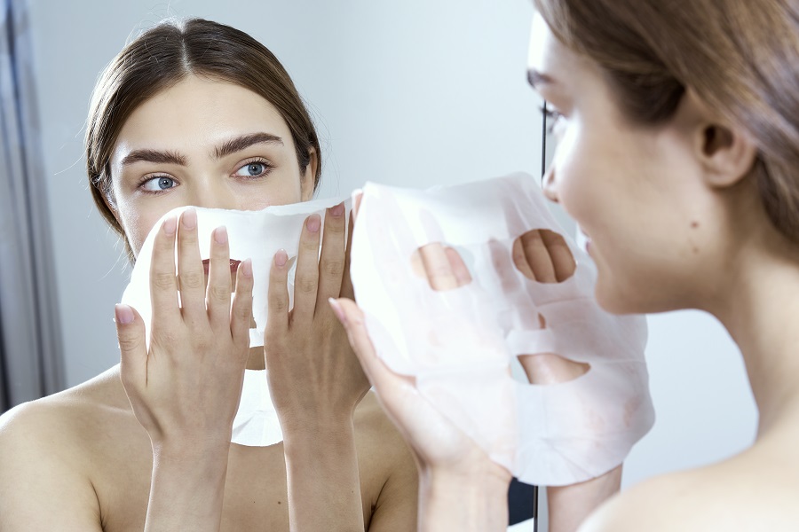 woman applying a sheet mask in the mirror 