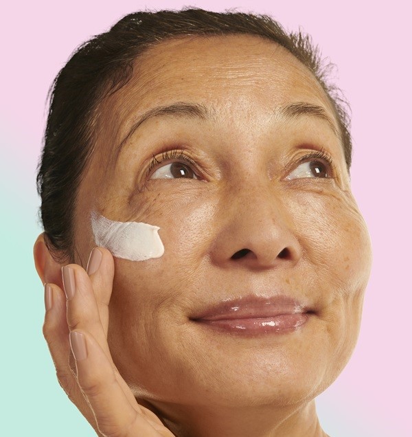 woman smiling applying moisturiser to cheeks 