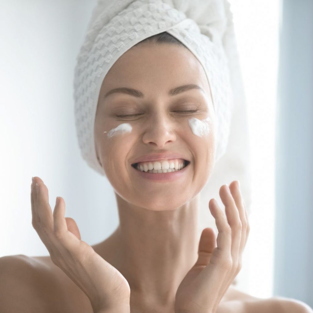 woman smiling applying moisturiser to face 